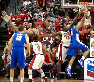 Students hold up a blown up sized poster of a UNLV basketball player as he guards and defends the hoop.