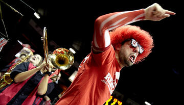 Close up of student cheering on hi team with band playing behind him.