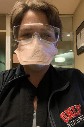 A woman wears a mask and a jacket emblazoned with "UNLV Nursing"
