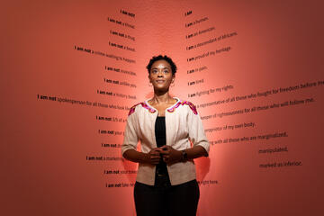 A woman stands in front of her art exhibit.