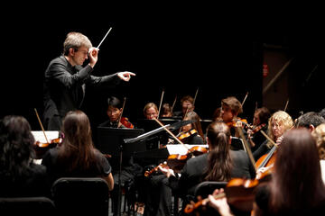 A conductor waves his baton in front of an orchestra