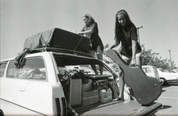 Two women unpacking a guitar from their vehicle.