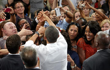 Back side aerial view of President Obama as he tries to handshake a group of people surrounding him.