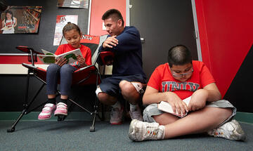 Student sitting by two young children who seem to be focused on what they are reading.