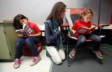 Student sitting between two younger children who are reading their books.