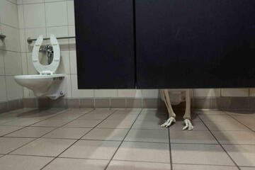 Skeleton feet visible from bottom of restroom stall