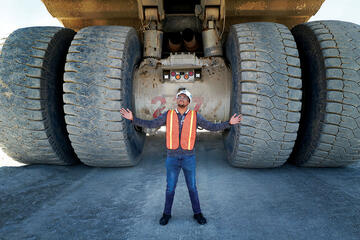Man in hardhat near massive mining truck.