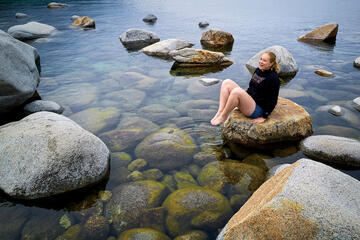 Woman on rock dipping toes in lake.