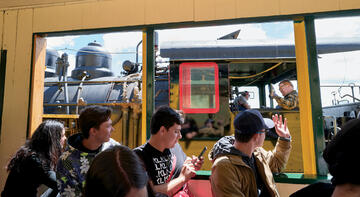 Group pictured from inside bus waving and passing train passengers.