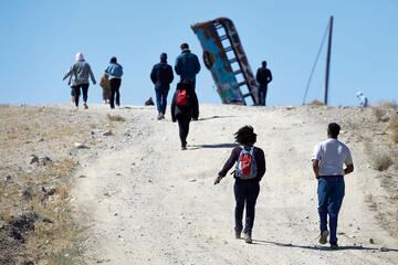 Group walking toward old bus standing on end in desert.