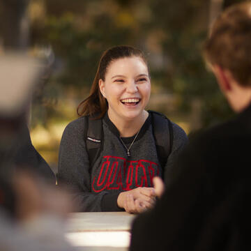 Kaila Seilder laughs with friends as they sit at a table. 