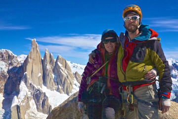 couple posing in climbing gear atop a mountain peak