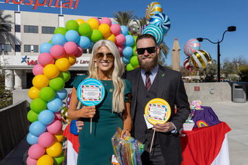 man and woman in front of rainbow arch holding lollipop signs