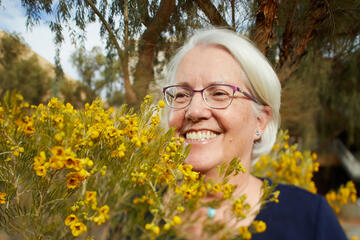 closeup of woman with gray hair and glasses behind a bush