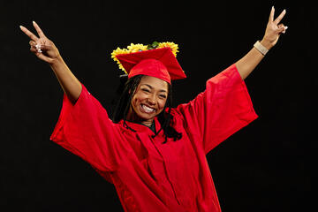 Woman in a red graduation cap and gown in front of a black background
