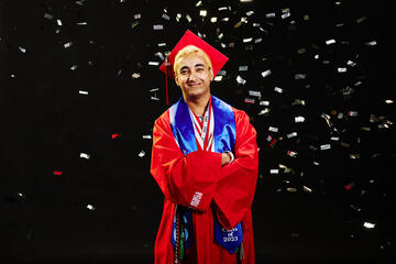 Man in a red graduation cap and gown with confetti falling