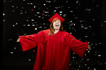 Woman in a red graduation cap and gown with confetti falling