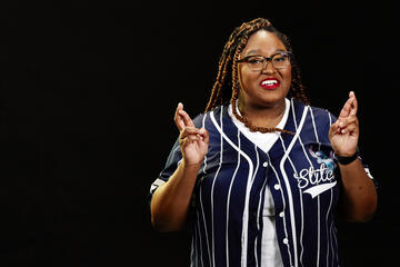 Woman in a blue baseball shirt in front of a black backround