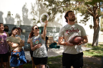 students outside in shadow under tree with one holding a disc and the other a football