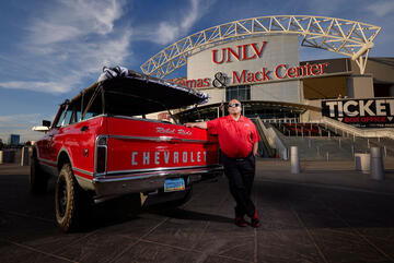 man posing next to classic car with events arena in background