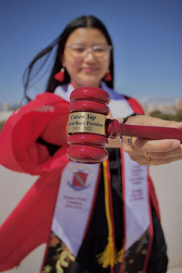 woman in graduation gown holding gavel that says "student body president"