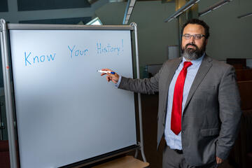 man pointing to whiteboard that reads: know your history