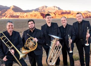 five individuals in desert setting holding various brass-wind instruments