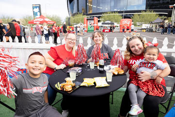 Family members wear white, red, and gray pom poms during a stadium tailgate