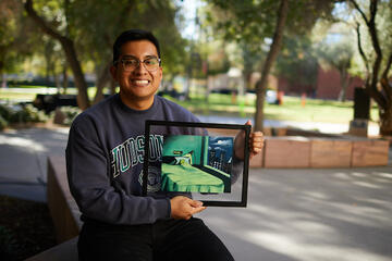 young man showing off framed art of a frog in a bed