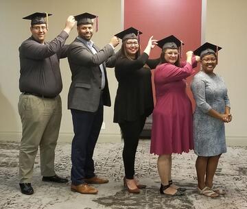five people in a line by height wearing graduation hats