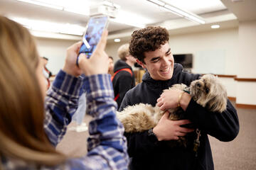 male student cradling a dog while other student takes photo