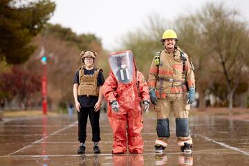 Three students in different first responder gear standing in the rain.