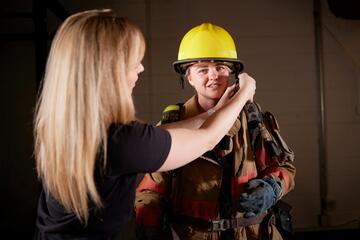 A kinesiology student puts on her first responder gear with the help of an instructor.