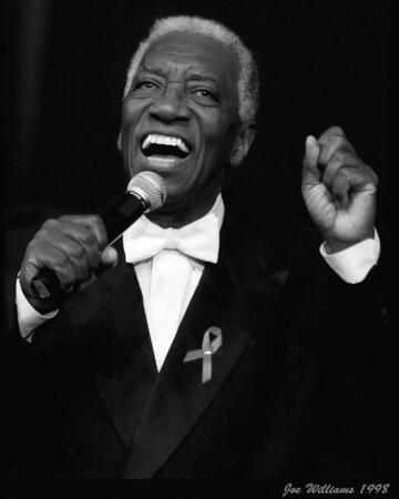 black and white photo of man in tuxedo singing with microphone