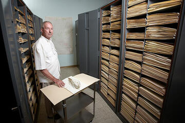 man standing next to file cabinets filled with images of herbs
