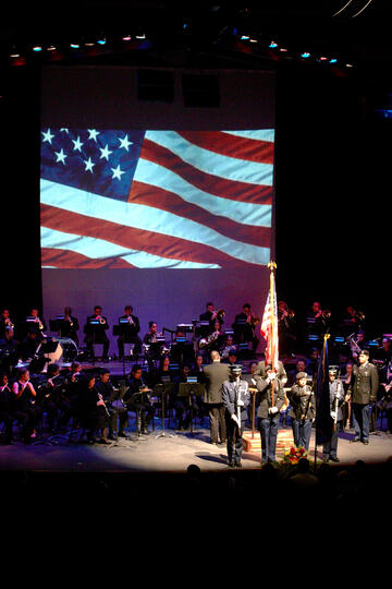 wind orchestra playing with a U.S. flag behind the stage
