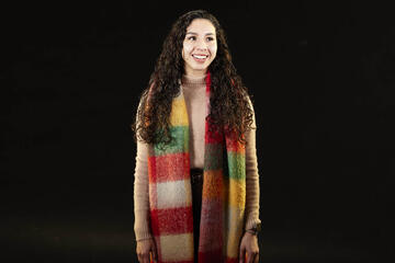 brown-haired female with colorful scarf around neck in front of black background