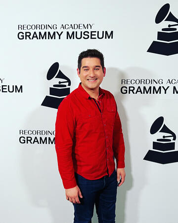 man in red shirt stands in front of Grammy backdrop