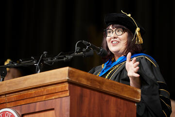 woman in graduation gown behind a podium
