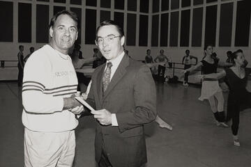 two men at check presentation with dancers in background