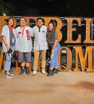 Four Rebel Events Board members in front of a large Rebel Homecoming sign