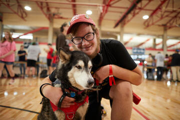 student in UNLV hat crouches while hugging sweet dog