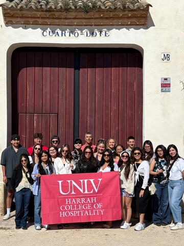 Hospitality College students traveling in Spain take a photo holding a flag with the Hospitality College logo.
