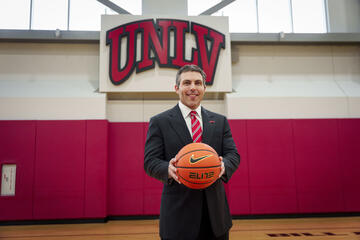 UNLV men's basketball coach Josh Pastner holds a basketball while posing in front of a UNLV logo at the Mendenhall Center