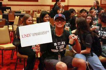 student holds a Harrah College of Hospitality sign