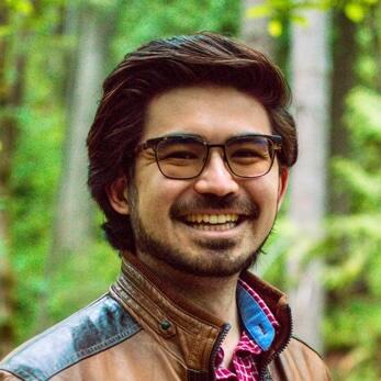 Thumbnail image of a smiling white male with dark hair and a beard wearing glasses and a brown leather jacket with red-and-white checkered collared shirt
