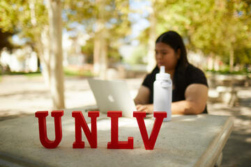 student at outside table on computer with UNLV mini letters at foreground