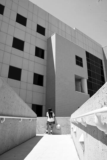 student with long hair at end of sidewalk in front of building