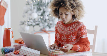 Young woman wearing sweater does online holiday shopping on laptop while holding credit card
