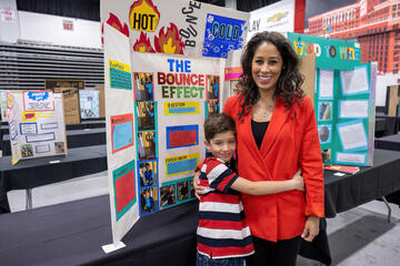 student hugs woman while standing in front of science project